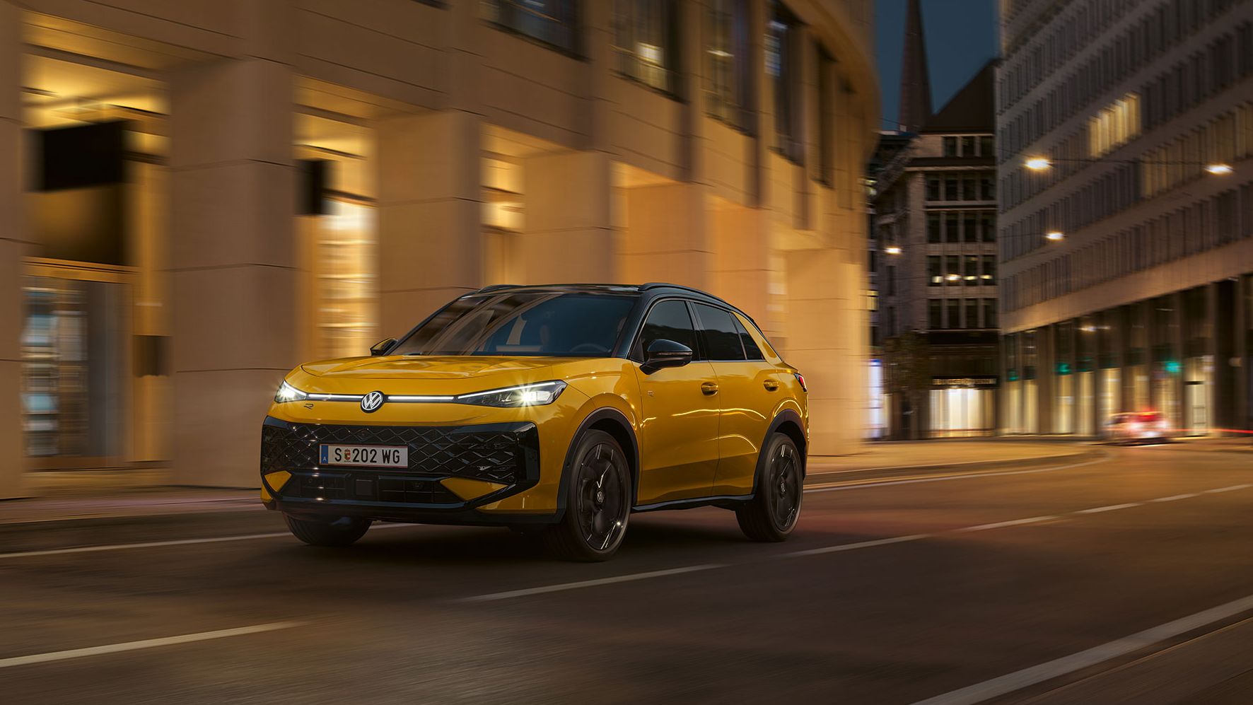 Ein gelber VW T-Roc R-Line fährt nachts durch eine urbane Umgebung.
