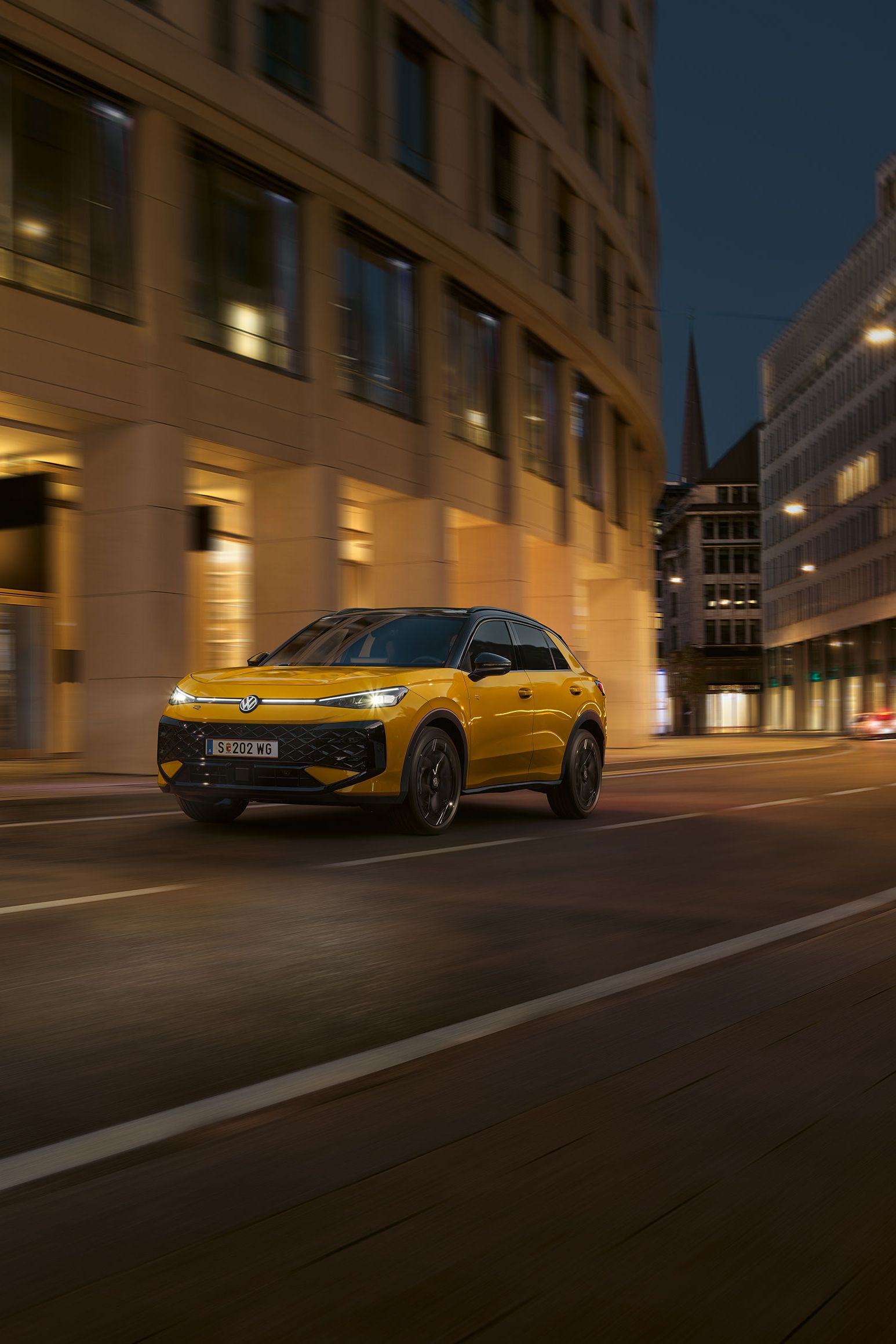 Ein gelber VW T-Roc R-Line fährt nachts durch eine urbane Umgebung.