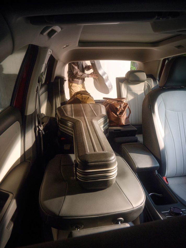 Das Bild zeigt das Innere eines T-Roc mit Ledersitzen. Auf dem Rücksitz liegt ein Gitarrenkoffer. Draußen steht eine Person mit einem weiteren Gitarrenkoffer in der Hand.