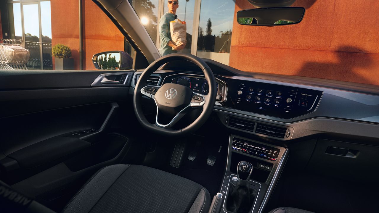 Interieur des VW Polo mit Infotainmentsystem, Multifunktionslenkrad und Digital Cockpit. Ein Mann läuft vor dem Auto entlang.