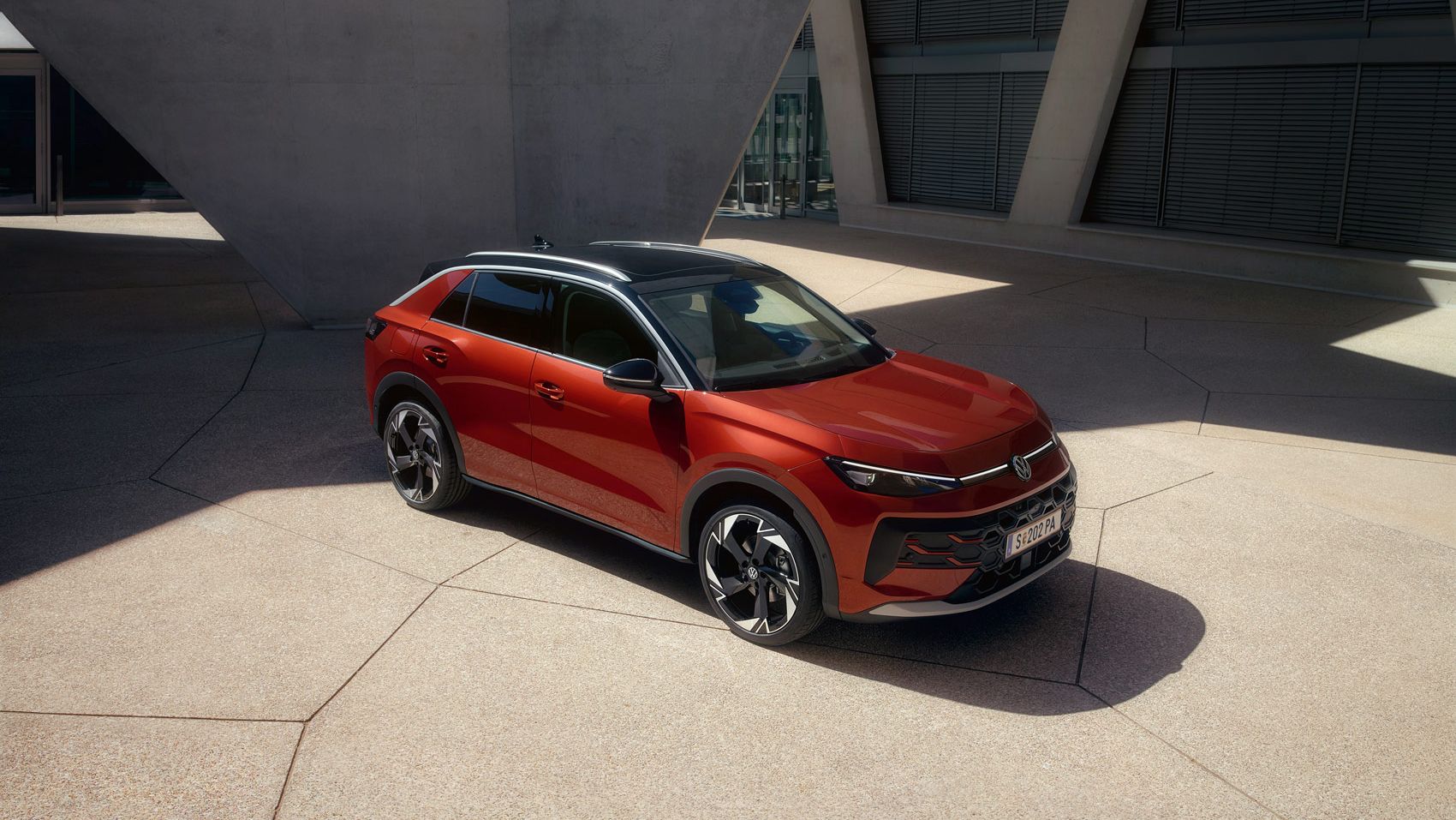 Ein roter VW T-Roc Style steht vor einem modernen Gebäude im Sonnenlicht