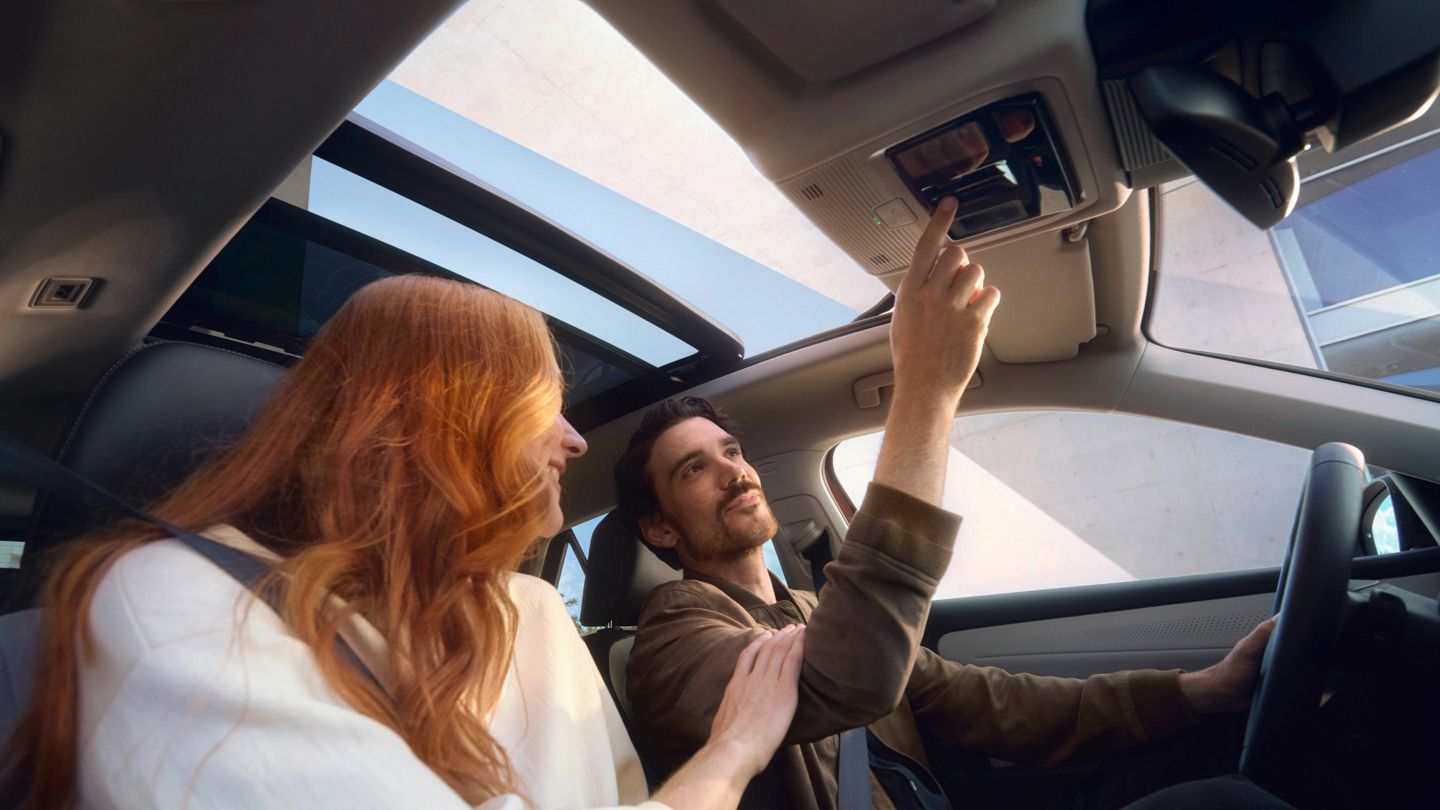 Zwei Personen sitzen im neuen VW T-Roc, eine davon hat rotes Haar und die andere betätigt eine Taste am Dach. Das Auto hat ein Panoramadach.