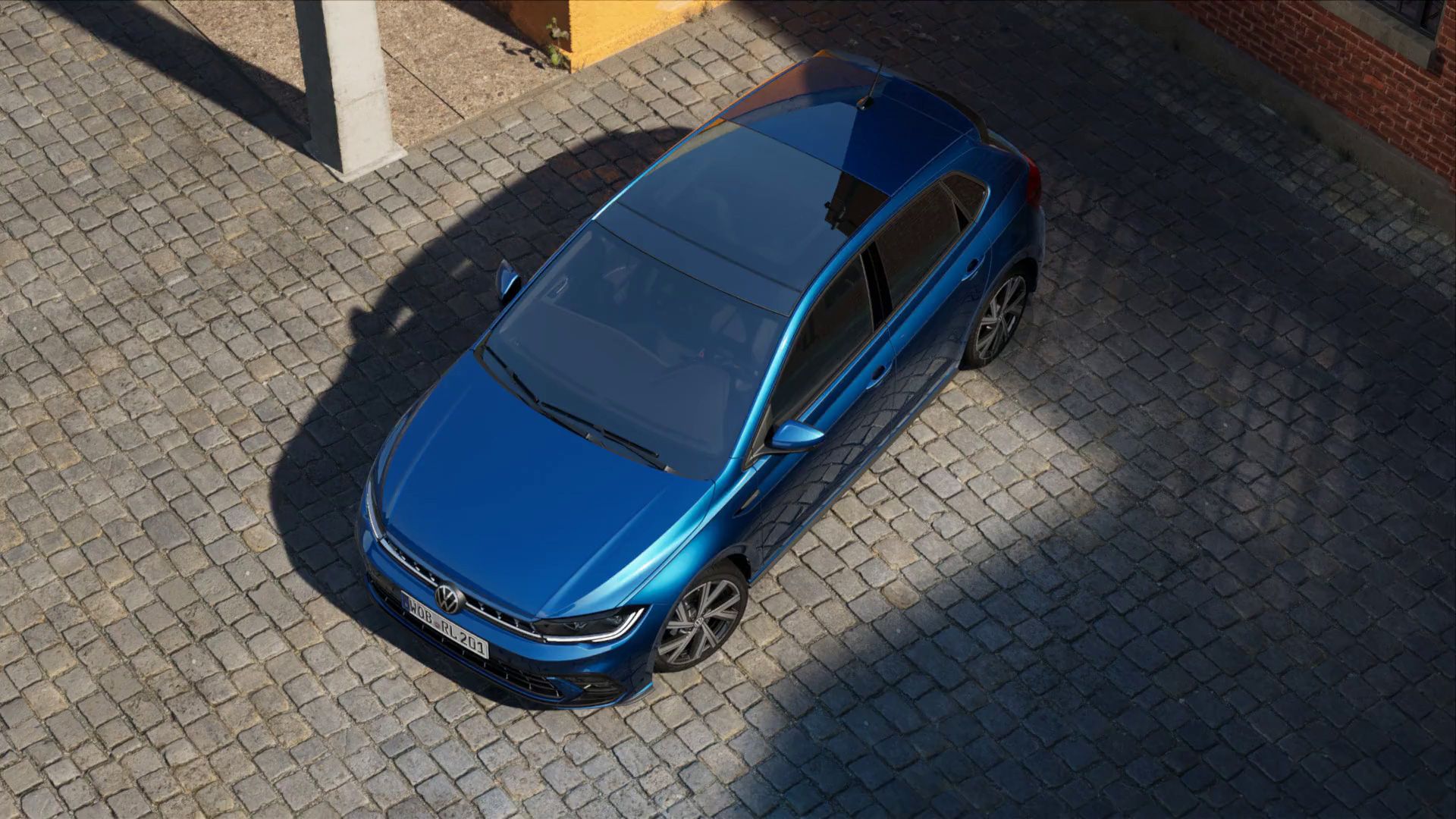 Ein blauer VW Polo steht auf einer Kopfsteinpflasterstraße, umgeben von Schatten und Sonnenlicht. Das Auto glänzt und hat reflektierende Stellen auf seiner Oberfläche. Im Hintergrund ist ein Teil eines Gebäudes sichtbar.