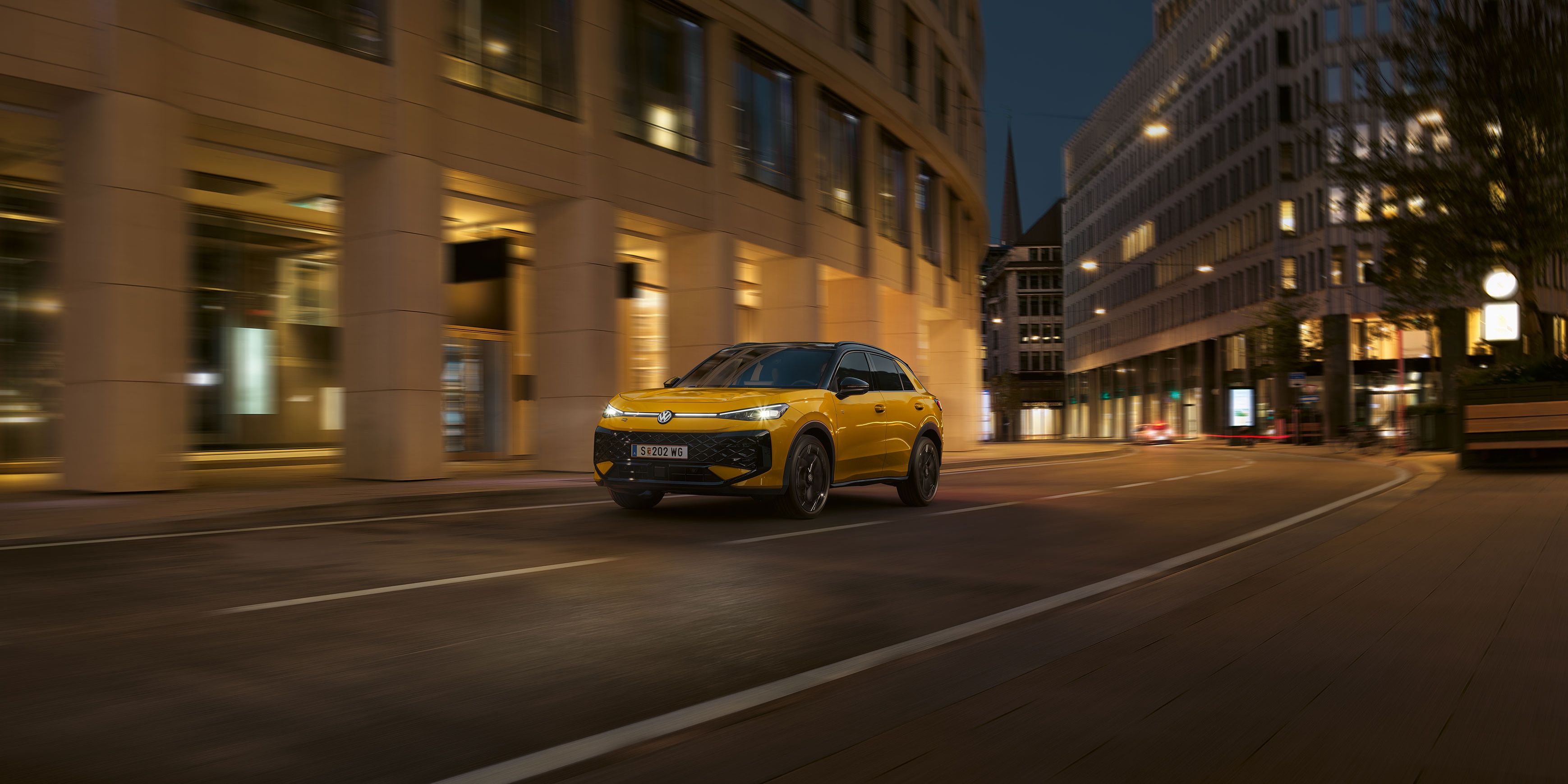 Ein gelber VW T-Roc R-Line fährt nachts durch eine urbane Umgebung.