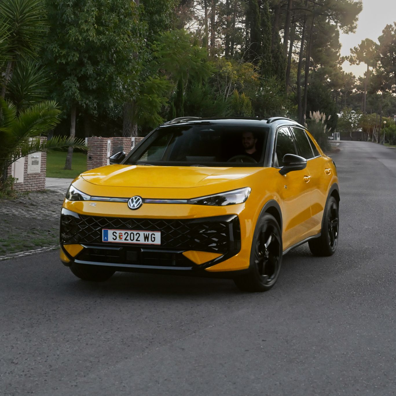 Ein gelber VW T-Roc R-Line fährt auf einer Straße durch eine bewaldete Umgebung.