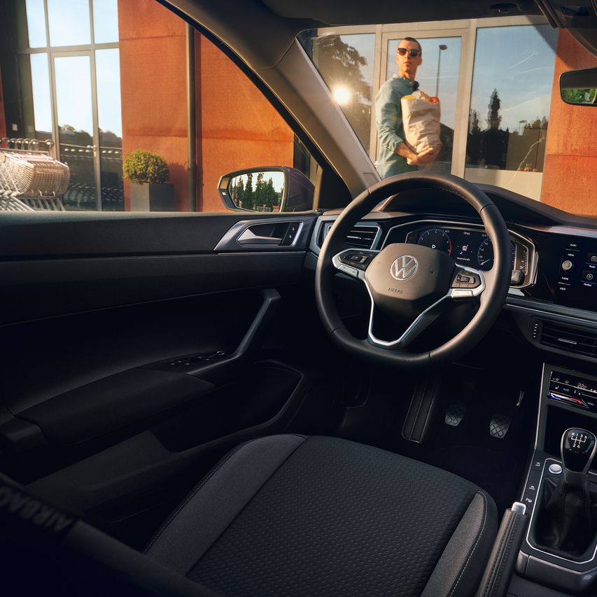 Interieur des VW Polo mit Infotainmentsystem, Multifunktionslenkrad und Digital Cockpit. Ein Mann läuft vor dem Auto entlang.