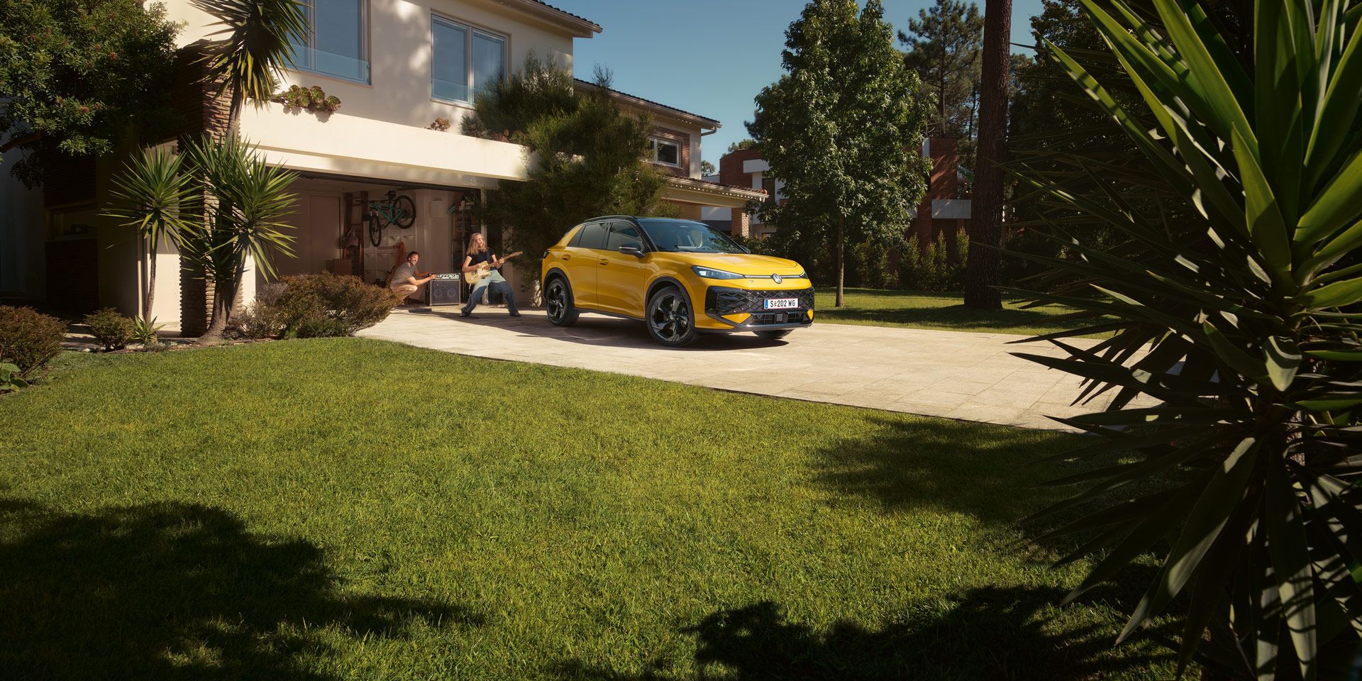 Ein gelber VW T-Roc R-Line steht vor der Garage, ein Mädchen spielt Gitarre, ihr Vater steuert den Lautsprecher.
