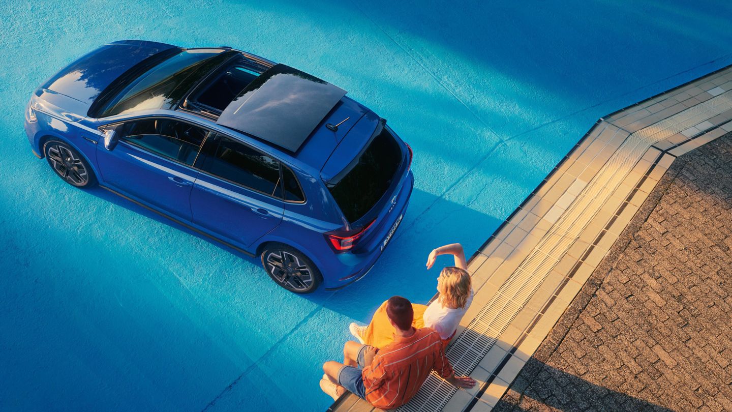 Der VW Polo R-Line mit geöffnetem Panoramadach steht in einem leeren Pool, zwei Personen sitzen am Rand des Pools.