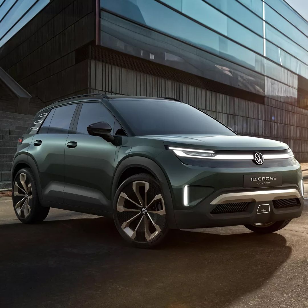 Ein dunkelgrünes Volkswagen ID. Cross steht auf einem Parkplatz vor einem modernen Gebäude mit Glasfassade. Der SUV hat futuristische Scheinwerfer und stylische Felgen. Im Hintergrund sind Treppenstufen und ein paar Palmen sichtbar.