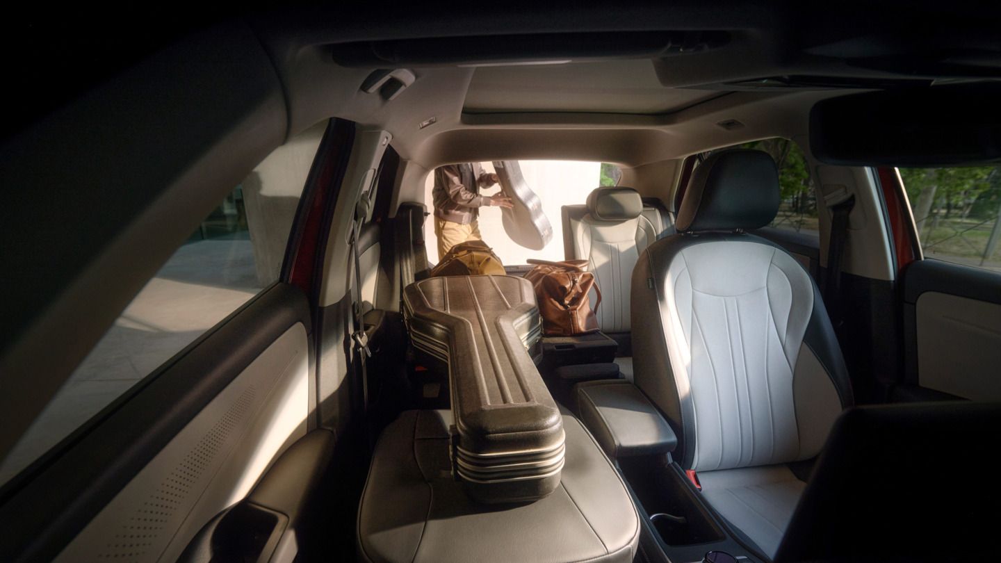 Das Bild zeigt das Innere eines T-Roc mit Ledersitzen. Auf dem Rücksitz liegt ein Gitarrenkoffer. Draußen steht eine Person mit einem weiteren Gitarrenkoffer in der Hand.