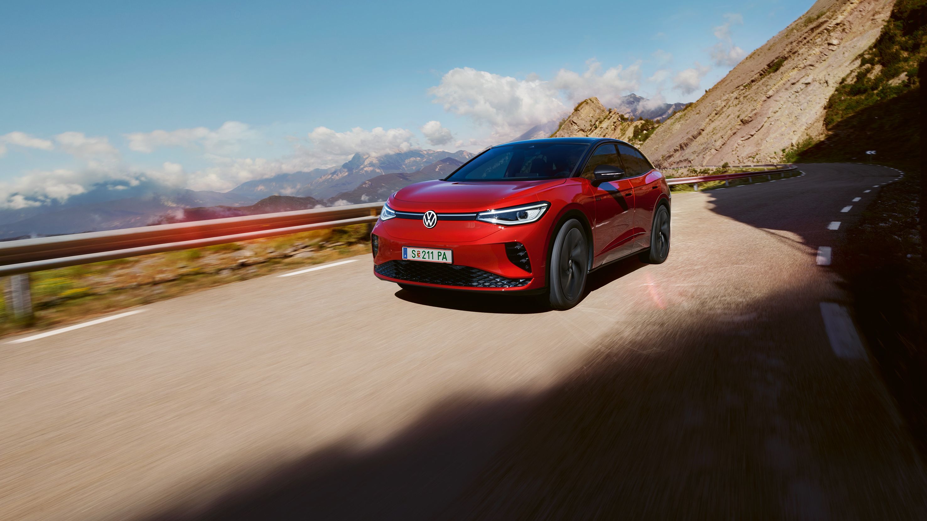 Roter VW ID.5 GTX fährt dynamisch auf einer Bergstraße. Blick auf Front, Räder und Seite.