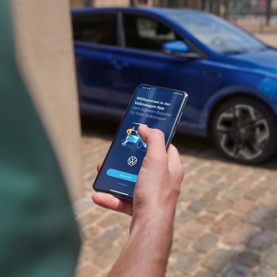 Ein blauer VW Polo steht auf einem Parkplatz. Eine Person prüft dessen Fahrdaten auf dem Smartphone.