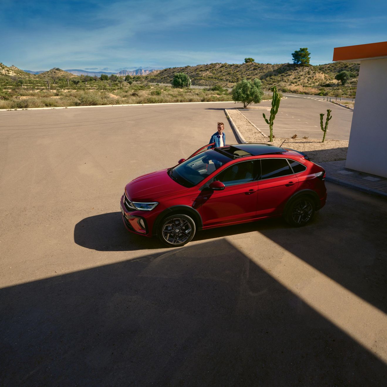 Mann steigt in den Beifahrersitz des geparkten roten VW Taigo ein mit geöffneten Schiebedach.